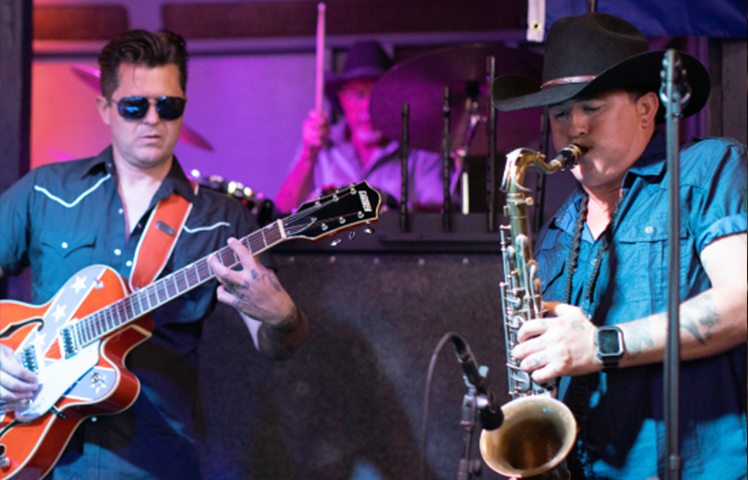 A man playing guitar and saxophone in front of other musicians.